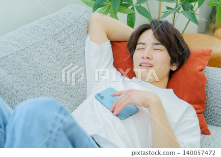 A young Japanese man sleeping on a sofa with his smartphone in his hand. A young Japanese man sleeping on a sofa with his smartphone in his hand. 140057472