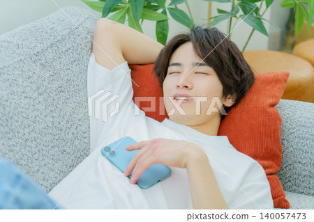 A young Japanese man sleeping on a sofa with his smartphone in his hand. A young Japanese man sleeping on a sofa with his smartphone in his hand. 140057473