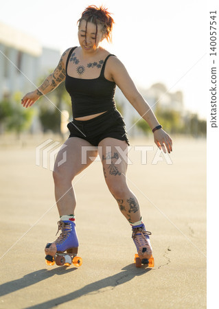 Tattooed woman happily roller skating outdoors Tattooed woman happily roller skating outdoors 140057541
