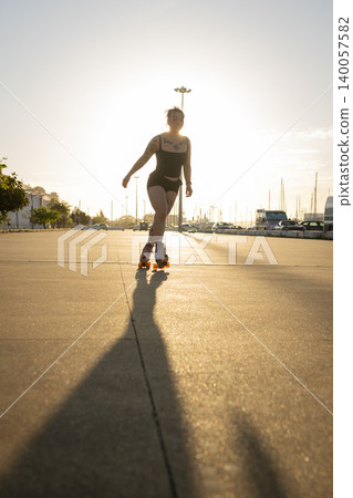 Young woman roller skating on urban street at sunset creating long shadow 140057582