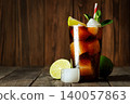 Cuba libre sparkling cola and rum cocktail is chilling in glass with condensation, ice, lime slices and fresh mint on weathered wooden surface 140057863