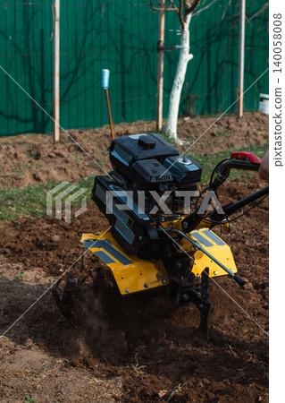 Man using walk-behind tractor to cultivate soil, preparing garden bed for planting, symbolizing agricultural work, spring preparation, and manual farming. Man using walk-behind tractor to cultivate soil, preparing garden bed for planting, symbolizing agricultural work, spring preparation, and manual farming. 140058008