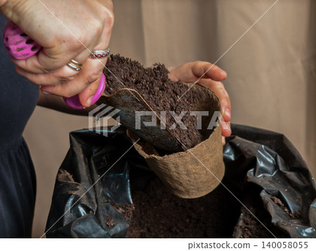 A woman's hands fill an organic, biodegradable peat pot with rich brown potting soil, preparing a seedling for transplanting - eco-friendly gardening, nurturing new life and growth.. A woman's hands fill an organic, biodegradable peat pot with rich brown potting soil, preparing a seedling for transplanting - eco-friendly gardening, nurturing new life and growth.. 140058055