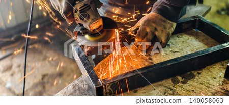 Worker using an angle grinder to cut and shape metal, producing a shower of bright orange sparks as part of the industrial fabrication process in a workshop environment. Worker using an angle grinder to cut and shape metal, producing a shower of bright orange sparks as part of the industrial fabrication process in a workshop environment. 140058063