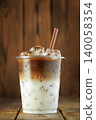 Refreshing iced latte coffee drink in transparent plastic cup with brown straw, ice cubes and condensation, staying cool and energizing on rustic wooden background 140058354