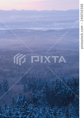 A fantastical winter scene in Nayoro, Hokkaido, with snow-covered mountains and trees, under a cloudy, dim twilight sky (January). A fantastical winter scene in Nayoro, Hokkaido, with snow-covered mountains and trees, under a cloudy, dim twilight sky (January). 140058388
