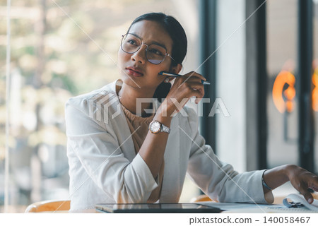 Thoughtful businesswoman holding pen and reviewing documents beside tablet, planning strategy and analyzing business data in bright office workspace with calm professional focus mindset. Thoughtful businesswoman holding pen and reviewing documents beside tablet, planning strategy and analyzing business data in bright office workspace with calm professional focus mindset. 140058467