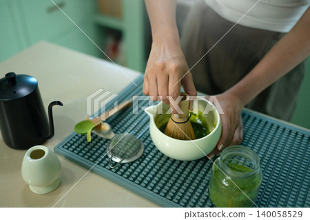 Close up of woman whisking matcha tea with bamboo chasen in kitchen Close up of woman whisking matcha tea with bamboo chasen in kitchen 140058529