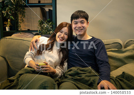 Smiling couple relaxing on sofa watching TV at home Smiling couple relaxing on sofa watching TV at home 140058533