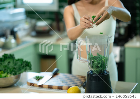 Closeup woman adding fresh kale into blender for healthy smoothie 140058545