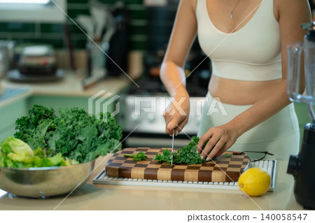 Cropped shot woman preparing fresh kale in modern green kitchen Cropped shot woman preparing fresh kale in modern green kitchen 140058547