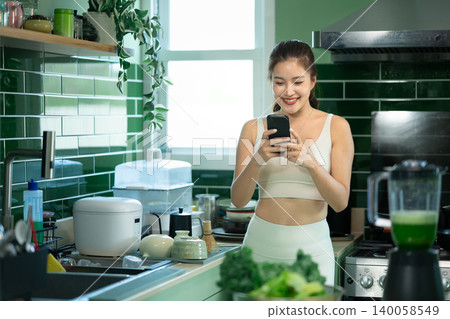 Woman checking smartphone after making green smoothie Woman checking smartphone after making green smoothie 140058549