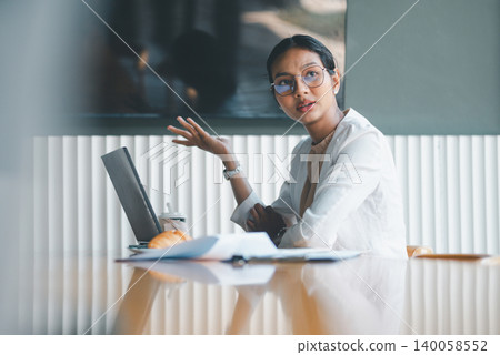 Businesswoman speaking beside laptop in office meeting, using hand gestures to explain ideas, ask questions and support discussion in a modern professional workspace setting. Businesswoman speaking beside laptop in office meeting, using hand gestures to explain ideas, ask questions and support discussion in a modern professional workspace setting. 140058552
