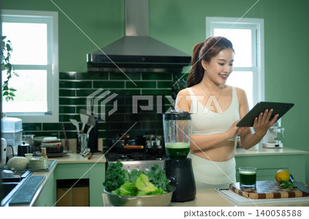 Fit woman using tablet in kitchen with green smoothie Fit woman using tablet in kitchen with green smoothie 140058588
