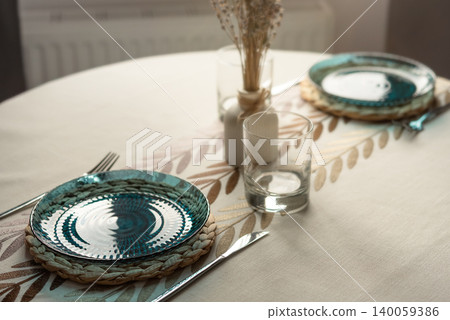 Cozy dining table setting with blue glass plates and soft sunlight Cozy dining table setting with blue glass plates and soft sunlight 140059386