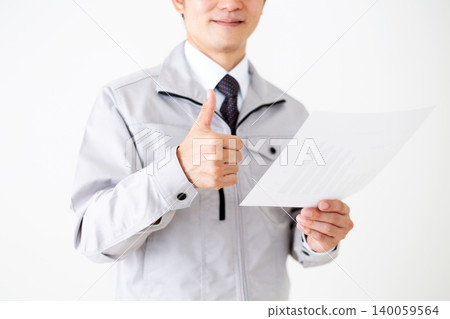 一位身穿灰色工作服的中年商人，在白色背景下看著圖表，做出了一個勝利的手勢。 140059564