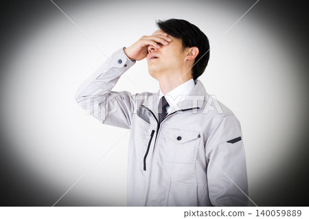 A middle-aged businessman in gray work clothes, covering his face and looking dejected, against a white background. A middle-aged businessman in gray work clothes, covering his face and looking dejected, against a white background. 140059889