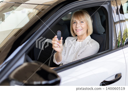 Happy senior woman holding car key while sitting inside newly purchased vehicle Happy senior woman holding car key while sitting inside newly purchased vehicle 140060519