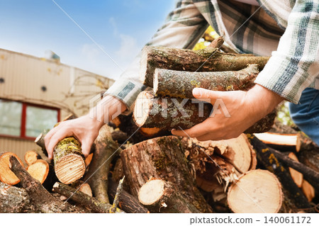 Man holding a stack of chopped wood logs and firewood in his hands. Concept of timber logging, lumber preparation, and rural winter heating. 140061172