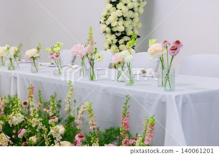 Wedding table is arranged with small vases of flowers for gathering in plain indoor space. Wedding table is arranged with small vases of flowers for gathering in plain indoor space. 140061201