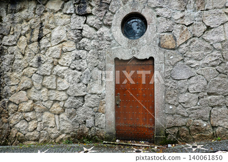 Vintage wooden door embedded in an ancient stone wall with a round window in Sintra, Portugal 140061850