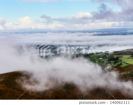 The foreground is a brown, grassy hillside with wisps of fog creeping down from above. The foreground is a brown, grassy hillside with wisps of fog creeping down from above. 140062111
