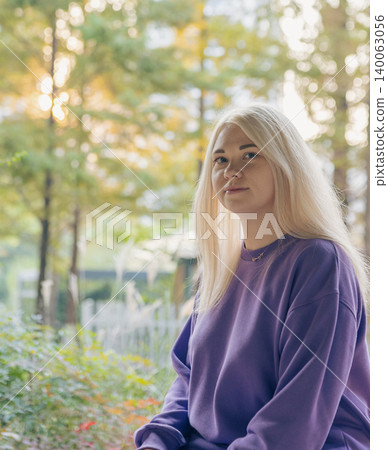 Young blonde woman in purple sweatshirt poses in outdoor park during a sunny afternoon Young blonde woman in purple sweatshirt poses in outdoor park during a sunny afternoon 140063056