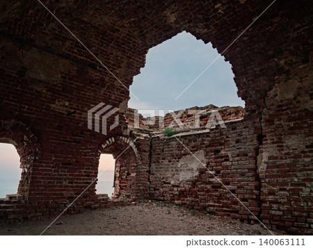 Ancient brick ruin interior with arched openings framing the ocean and evening sky 140063111