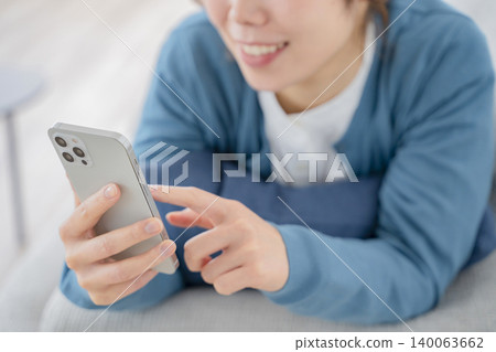 一位女士在沙發上放鬆時看著智慧型手機 一位女士在沙發上放鬆時看著智慧型手機 140063662