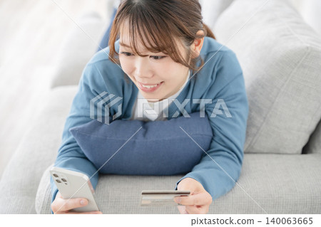 一位女士在沙發上放鬆時看著智慧型手機 一位女士在沙發上放鬆時看著智慧型手機 140063665