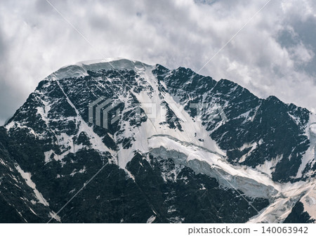 High altitude mountain range featuring steep, dark rock faces covered with extensive snow and ice. 140063942