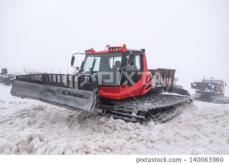 Red snow groomer parked on a snow-covered mountain slope during a foggy winter day 140063960