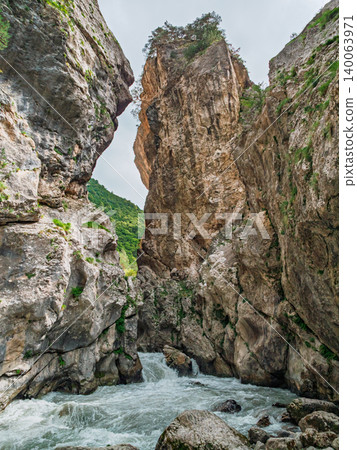 Towering rock walls surround a rushing river in a spectacular mountain gorge during daytime Towering rock walls surround a rushing river in a spectacular mountain gorge during daytime 140063971