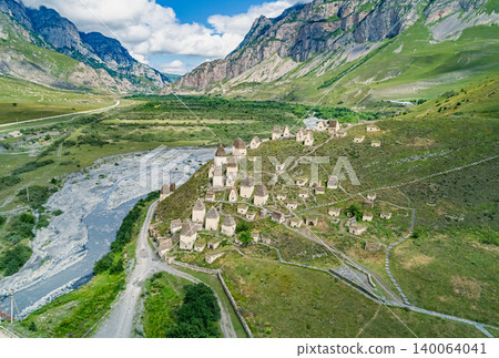 Aerial view captures Dargavs City of the Dead sit on a hill near a river with mountains in the background during a sunny day in North Ossetia-Alania Aerial view captures Dargavs City of the Dead sit on a hill near a river with mountains in the background during a sunny day in North Ossetia-Alania 140064041