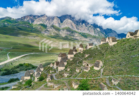 Aerial view captures Dargavs City of the Dead sit on a hill near a river with mountains in the background during a sunny day in North Ossetia-Alania Aerial view captures Dargavs City of the Dead sit on a hill near a river with mountains in the background during a sunny day in North Ossetia-Alania 140064042