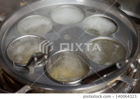 A scene of boiling noodles in a strainer in a large boiling pot at a local Chinese restaurant. A scene of boiling noodles in a strainer in a large boiling pot at a local Chinese restaurant. 140064323