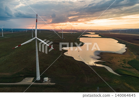 Aerial view of a wind turbines generate clean energy during sunset over a tranquil lake in a rural landscape with open fields Aerial view of a wind turbines generate clean energy during sunset over a tranquil lake in a rural landscape with open fields 140064645