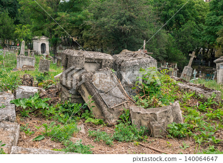 Crumbling stone monuments scattered across ancient overgrown cemetery during daylight hours 140064647