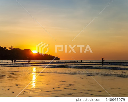 People Silhouetted on Tropical Beach at Golden Sunset with Sun Reflection on Wet Sand People Silhouetted on Tropical Beach at Golden Sunset with Sun Reflection on Wet Sand 140065979