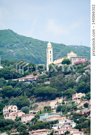 A church with a large tower stands atop a hill where houses are clustered on the slopes, on the French island of Corsica in the Mediterranean Sea. 140066302