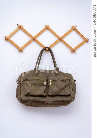 Brown snakeskin pattern leather handbag on wooden rack. Khaki texture duffel bag hanging on white wall Brown snakeskin pattern leather handbag on wooden rack. Khaki texture duffel bag hanging on white wall 140066371