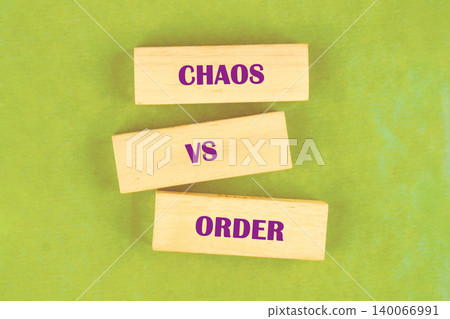 Three rectangular wooden blocks are arranged on a bright green surface, forming a conceptual stack. The words CHAOS, VS, and ORDER are printed on the blocks in purple text Three rectangular wooden blocks are arranged on a bright green surface, forming a conceptual stack. The words CHAOS, VS, and ORDER are printed on the blocks in purple text 140066991