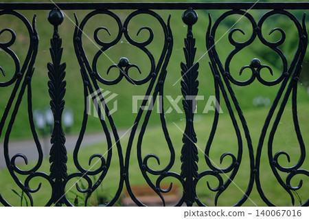 Close up of an antique black wrought iron fence displaying ornate scroll patterns and vertical leaf-like elements Close up of an antique black wrought iron fence displaying ornate scroll patterns and vertical leaf-like elements 140067016