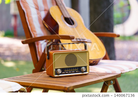 Outdoor garden relaxation area with wooden chair acoustic guitar and vintage radio leisure scene Outdoor garden relaxation area with wooden chair acoustic guitar and vintage radio leisure scene 140067136