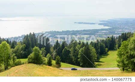 High angle view of a car driving on a rural road through green hills and forests in Germany. Landscape overlooking Lake Constance. Summer Bodensee concept High angle view of a car driving on a rural road through green hills and forests in Germany. Landscape overlooking Lake Constance. Summer Bodensee concept 140067775