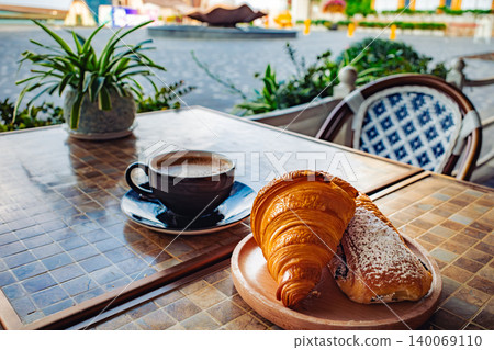 A breakfast set of coffee and a croissant is placed on a table on the terrace. A breakfast set of coffee and a croissant is placed on a table on the terrace. 140069110