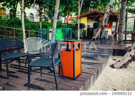 A view of palm trees and the terrace seating of an outdoor cafe near a tropical beach. 140069112