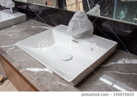 White Kohler ceramic basin sink installed on dark gray countertop. White Kohler ceramic basin sink installed on dark gray countertop. 140070820