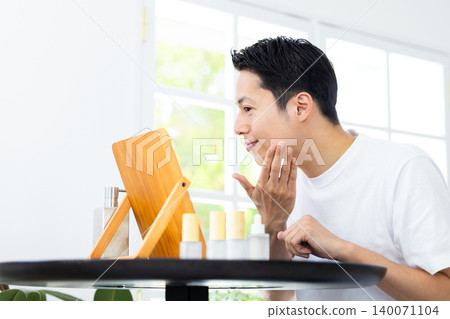 Beauty image: A man doing skincare while looking in a mirror. 140071104