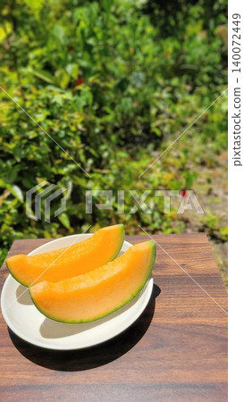 Fresh, juicy red-fleshed cut melons arranged on a white plate, photographed outdoors amidst the beautiful fresh greenery. Fresh, juicy red-fleshed cut melons arranged on a white plate, photographed outdoors amidst the beautiful fresh greenery. 140072449